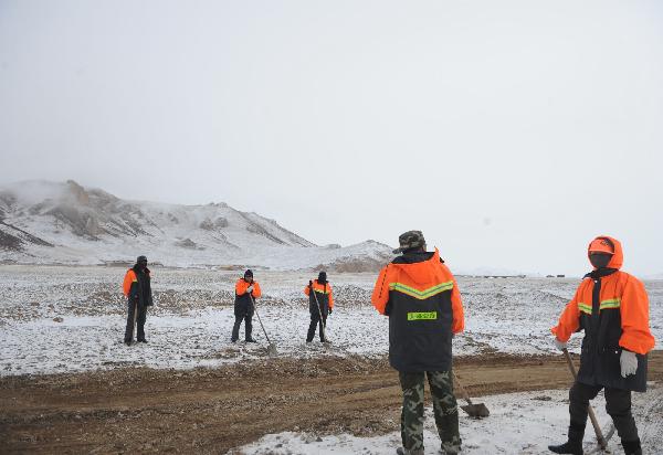 Road workers pave the way for a long fleet of cargo vehicles transporting quake-relief materials to Yushu, northwest China's Qinghai Province, April 19, 2010. The quake-relief materials were continuously transported to the disaster areas despite the snowfall and frozen road surface.