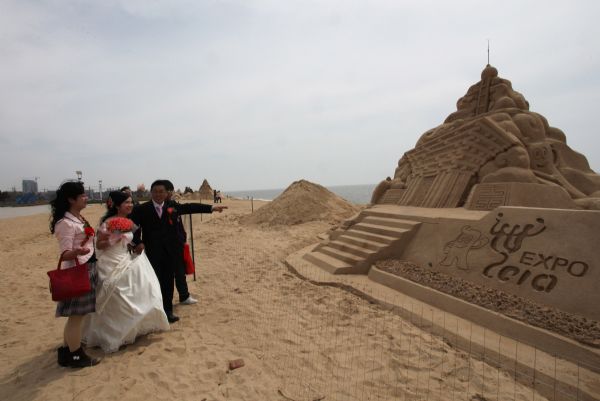 A newly-wedded couple is seen beside the sand sculpture work in the theme of the Shanghai World Expo on the beach in Wendeng City, east China's Shandong Province, April 25, 2010.