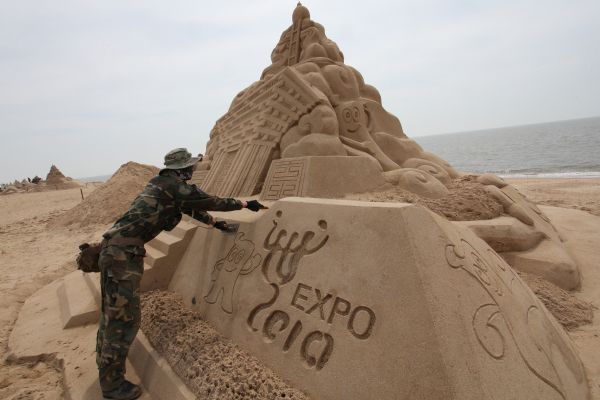 A sand sculpture artist and a worker finish the sand sculpture work in the theme of the Shanghai World Expo on the beach in Wendeng City, east China's Shandong Province, April 25, 2010. 