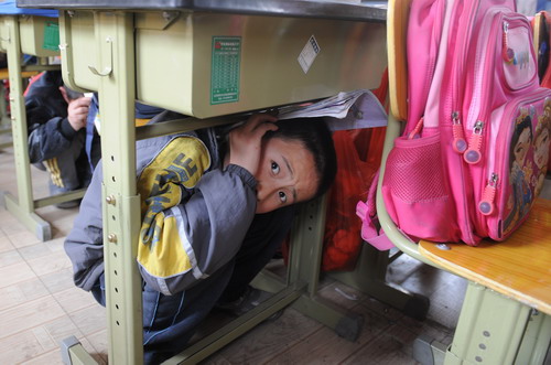 Students cover their heads and necks with their arms hiding underneath desks in a safety drill at a school in Shijingshan district in Beijing, on April 27, 2010. 