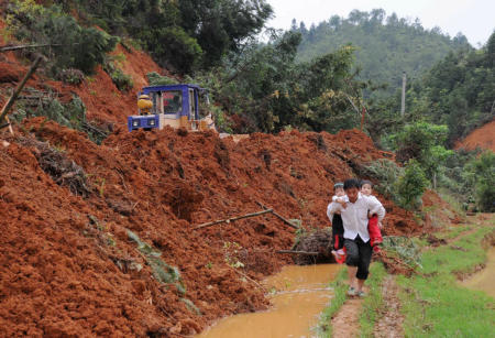 A villager carrying two children walks Sunday along a muddy road covered by a landslide in Nanding County, Jiangxi Province.