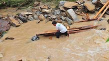 A man tries to take back wood pieces in flood in Cangwu County of southwest China's Guangxi Zhuang Autonomous Region, June 16, 2010.