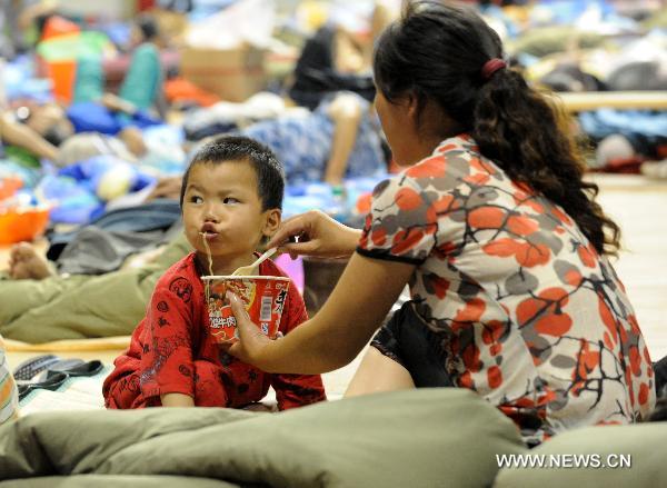 A mother affected by floods helps her son eat instant noodles in a gymnasium serving as an evacuation center in Wuzhou City of east China's Jiangxi Province, June 23, 2010.