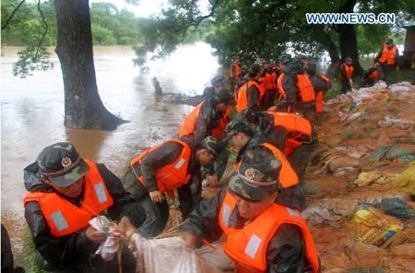 A contingent of armed policemen with the Ji'an City's Detachment convey and pile up sand bags in a rush consolidation of the Fangzhou Batardeau to contain the tempestuous and surging Ganjiang River, at Liujiacun section, in Ji'an City, east China's Jiangxi Province, June 24, 2010.