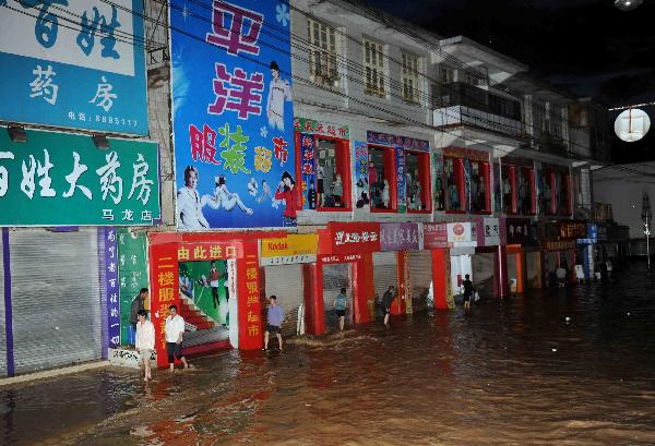 People wade through floodwaters in front of some stores in Malong County of southwest China's Yunnan Province June 26, 2010. 