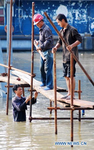 Three workers put up the frame of makeshift passage through the flooded street, at the sluice gate No. 28 on the up-surging Yangtze River at the section of Jiujiang, east China's Jiangxi Province, June 27, 2010.