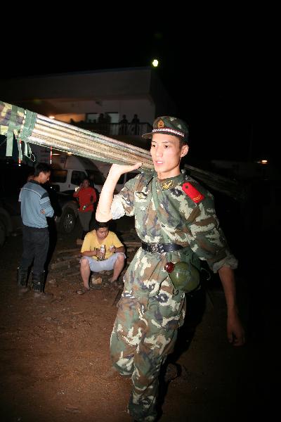 An armed policeman carries on shoulder poles for propping up the makeshift shelter during the rescue in Dazhai Village, Gangwu Township, of Guanling Bouyei and Miao Autonomous County, southwest China&apos;s Guizhou Province, June 28, 2010.
