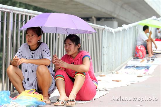 Two women sit on the street with an umbrella in hand to shield themselves from the sun in Beijing on July 4, 2010. The strongest heat wave so far this summer hit the city on Sunday, with the temperature at noon above 35 degrees Celsius. The city's meteorological center has issued this year's first yellow-coded heat alert for Sunday, warning the heat wave will continue for the next three days. [China Daily/Asianewsphoto]