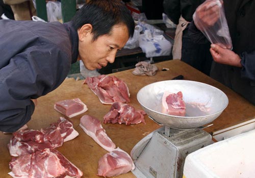 A man checks the scales before buying a piece of pork at a market in Beijing. Rising pork prices may be a source of uncertainty in the second half of the year.