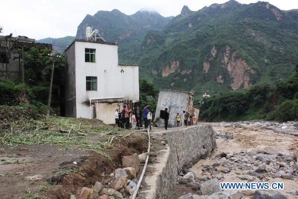 Local residents stand outside damaged houses after the ravage of flash floods in Xiaohe Township of Qiaojia County, Zhaotong City, southwest China's Yunnan Province, July 13, 2010. 