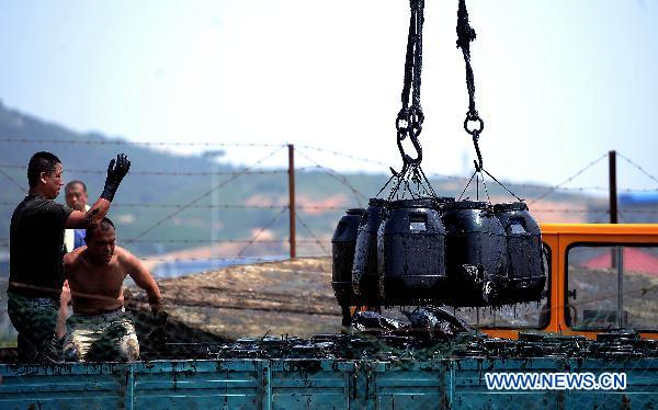 Workers transport barrels of crude oil during the oil spill cleanup operation near Xingang Harbor in Dalian City, northeast China's Liaoning Province, July 25, 2010. 