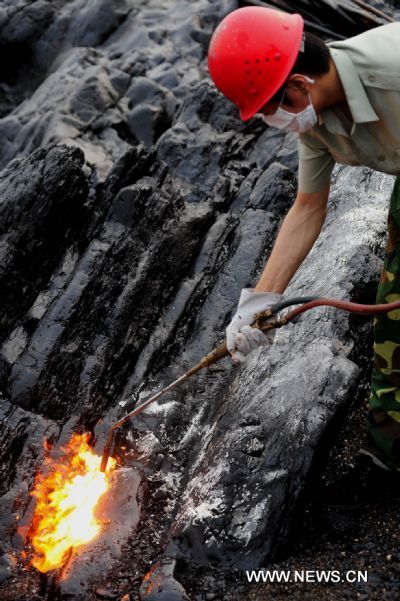 A worker cleans the reefs at Xieziwan bay in Dalian, northeast China&apos;s Liaoning Province, July 30, 2010. Industrial cleaners and gas welding blowpipes were devoted to clean the reefs after the oil pipe explosion at Dalian Xingang Harbor. (Xinhua/Ma Yidong) (ly) 