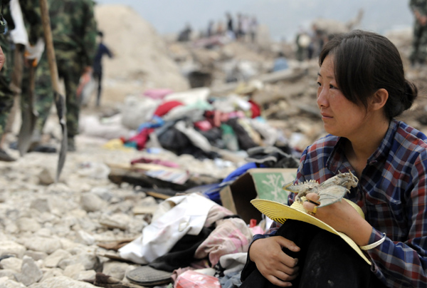 Hui Guoqin holding her father's belongings waits on ruins and wish for the good news of her missing parents and sister-in-law in the landslides-hit Zhouqu County, Gannan Tibetan Autonomous Prefecture in northwest China's Gansu Province, Aug. 11, 2010. 