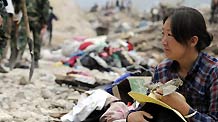 Hui Guoqin holding her father's belongings waits on ruins and wish for the good news of her missing parents and sister-in-law in the landslides-hit Zhouqu County, Gannan Tibetan Autonomous Prefecture in northwest China's Gansu Province, Aug. 11, 2010.