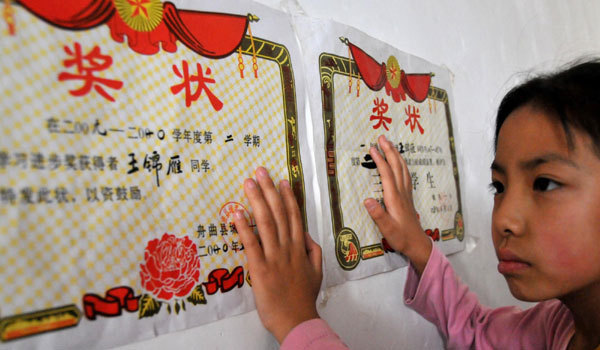 Wang Jinyan, 8, who excels in school, looks at her awards. She is a student from No 1 Primary School in mudslide-hit Zhouqu, northwest China's Gansu Province.