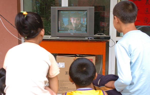 Children watch TV outside their makeshift settlement in mudslide-hit Zhouqu, northwest China's Gansu Province. Some 1,000 TV sets were installed recently in three settlements in Zhouqu, China Daily reported.