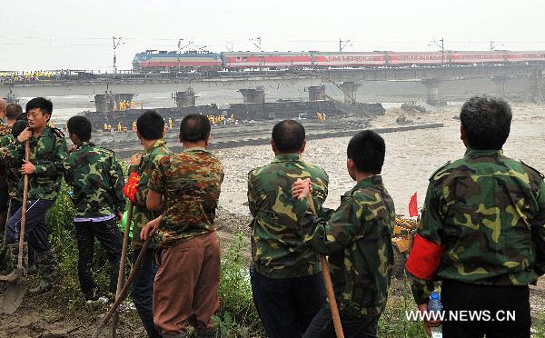 Workers look at a train running on the Baoji-Chengdu Railway in Xiaohan Township of Guanghan, a city of Sichuan Province, Aug. 20, 2010.