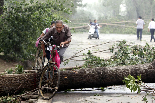 A girl helps an old man carry his bicycle across a tree blown down by a storm in Luoyang on Sept 4. Storms swept Luoyang, central China's Henan Province from 7:00 AM Saturday. 
