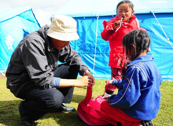 Gelhaigyu Gyaco of Tibetan ethnic group repairs a schoolbag for a student beside a tent classroom in Zhamang of Batang Village, Yushu Tibetan Autonomous Prefecture, northwest China's Qinghai Province, on Aug. 25, 2010. 