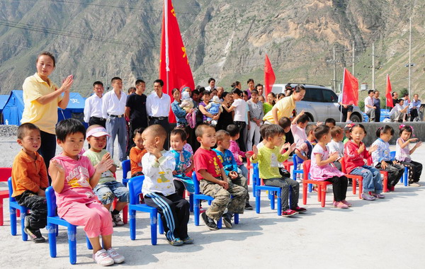 Kids and their parents attend an opening ceremony of a newly-built kindergarten for victims of mudslide-hit Zhouqu, Gansu Province on September 14, 2010. The makeshift kindergarten serves as a simple but important education institution for kids of families in the disaster-battered area.