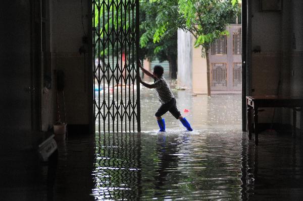 A woman opens the gate of her flooded home in Qionghai, south China's Hainan Province, Oct. 17, 2010. Heavy rainfall hit Qionghai again on Sunday. 