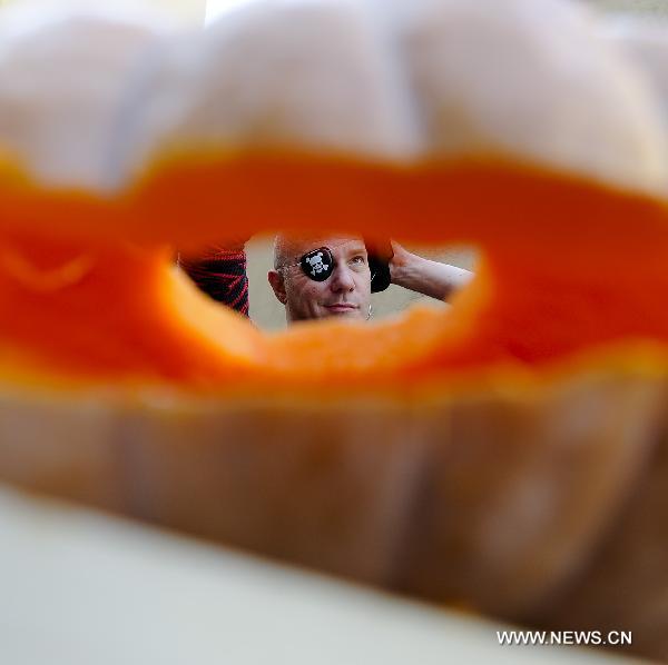 A man poses for a photo through the eye of a traditional Jack-o'-lanterns during a small gathering in Los Angles, the United States, Oct. 23, 2010. 