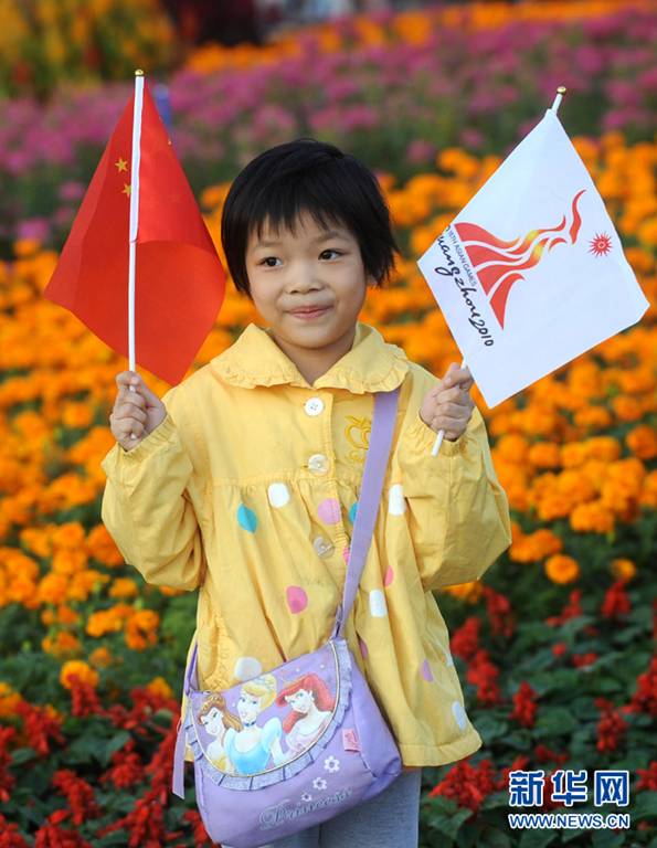 A little girl takes a photo with a national flag and an Asian Games flag in Guangzhou, southeast China&apos;s Guangdong Province. Guangzhou has dressed up itself with flowerbeds, sculptures and mascots to embrace the upcoming grand festival. 