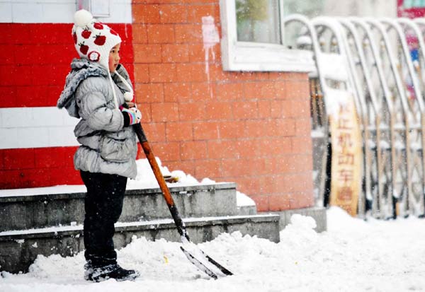 A child takes a break after shoveling snow in Harbin. [Xinhua]