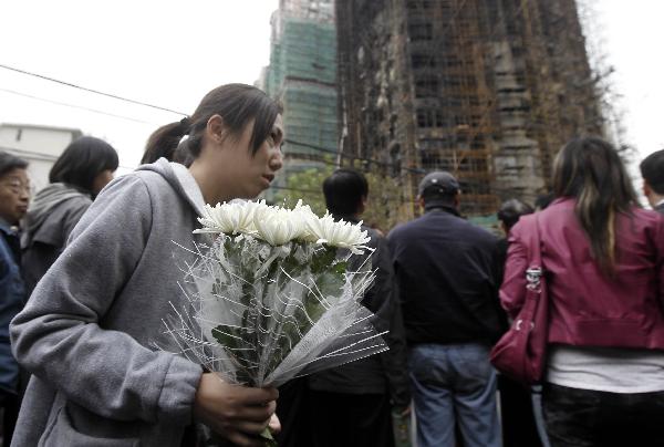 A girl presents flowers to the accident site to mourn for fire victims in Shanghai, east China, Nov. 16, 2010. The death toll of a big fire that engulfed the high-rise building in downtown Shanghai had risen to 53 by 9:30 a.m. Tuesday, local authorities said. [Xinhua] 
