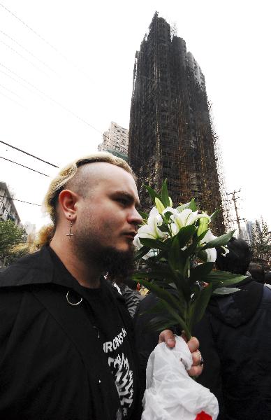 A young man from Russia presents flowers to the accident cite to mourn for fire victims in Shanghai, east China, Nov. 16, 2010.The death toll of a big fire that engulfed the high-rise building in downtown Shanghai had risen to 53 by 9:30 a.m. Tuesday, local authorities said. [Xinhua]