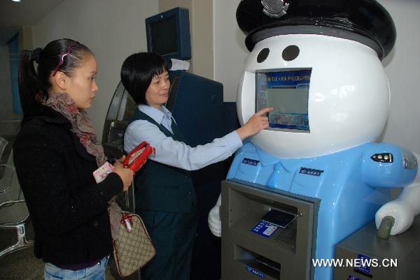 A staff member helps a resident to use the exit and entry service robot named 'A Pang' in Quanzhou City's exit and entry administration, southeast China's Fujian Province, Nov. 24, 2010.