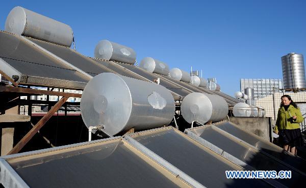 Photo taken on Dec. 4, 2010 shows a woman checking tanks of solar water heater atop a residential building in Kunming, capital of southwest China&apos;s Yunan Province. 