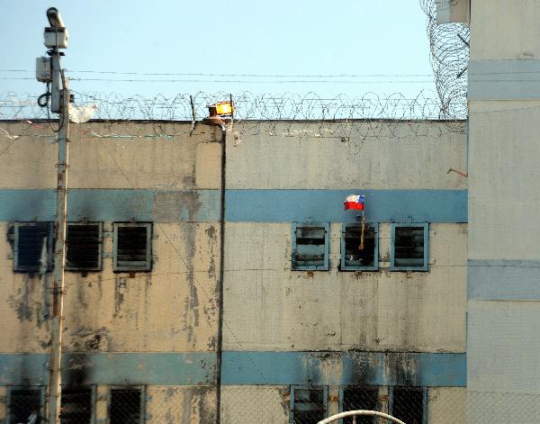 An inmate waves a Chilean flag from inside San Miguel public prison, after a fire broke out in the building, killing 81 inmates, in Santiago December 8, 2010. [Xinhua]