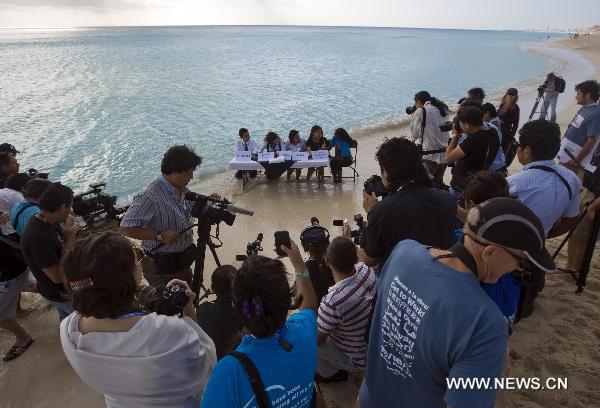 Activists from the 350.org environmental protection NGO sit on a table partially submerged in water as they pretend to represent countries taking part in the UN climate talks during a staged news conference at a beach in Cancun, Mexico, Dec. 9, 2010. 