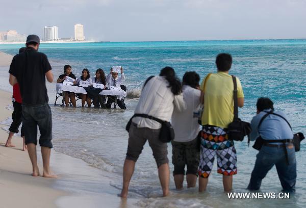 Activists from the 350.org environmental protection NGO sit on a table partially submerged in water as they pretend to represent countries taking part in the UN climate talks during a staged news conference at a beach in Cancun, Mexico, Dec. 9, 2010. 