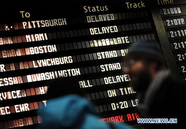 Commuters walk past a screen showing the train information at Pennsylvania Station in Manhattan of New York, the United States, Dec. 27, 2010. 