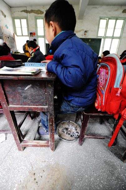 A makeshift hand-stove is placed under a student's seat at a school in Chaping township, Xinhuang Dong Autonomous County in central China's Hunan Province, Jan 6, 2011.