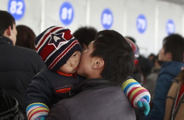A man with a baby in his arms waits in the line to buy train tickets in Shanghai, east China, Jan. 9, 2011. 
