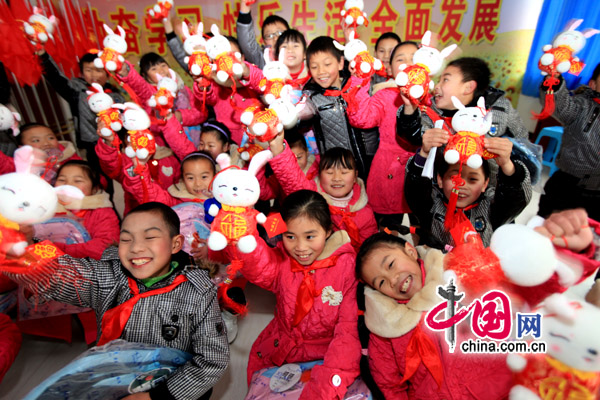 Children of migrant workers show off their new cotton-padded jackets and rabbit toys. [China.com.cn]