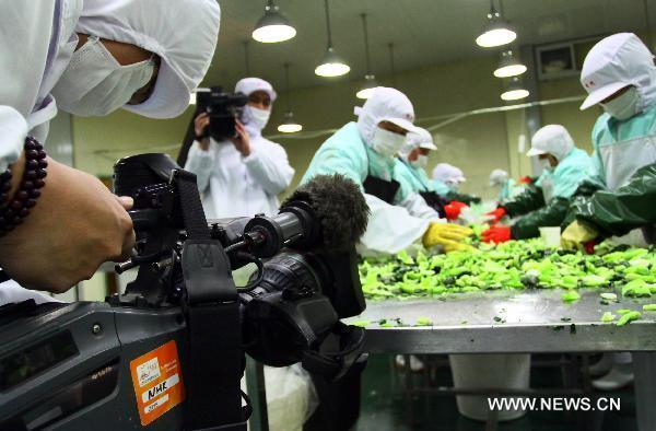 A journalist from NHK (Japan Broadcasting Corporation) shoots as the workers work on the production line at a food factory in Jiashan of east China&apos;s Zhejiang Province, March 24, 2011. 