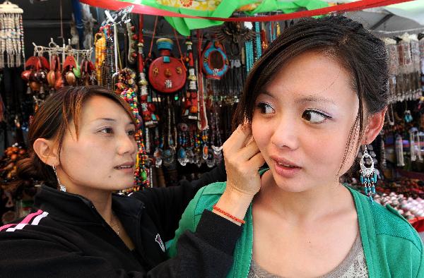 A girl (R) tries a pair of earrings in a shop on Barkhor Street in Lhasa, capital of southwest China's Tibet Autonomous Region, July 24, 2011.