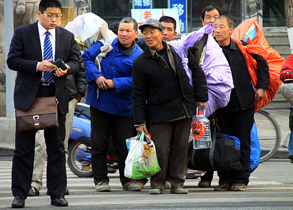 Migrant workers carrying packages wait to cross the street in Ji'nan, Shandong Province, on Wednesday. 