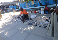 An old man is selling used mobile phones accessories like batteries, housing and headphones near the airport.