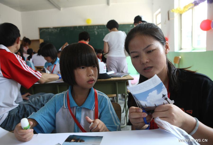 Primary school student Wu Manjie (L) is helped by a volunteer to cut a picture from a magazine to patch a big picture about her dream during a charitable activity in Shuren School, a school for the children of migrant workers, in Beijing, capital of China, Aug. 12, 2012. 