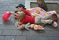 Three kids are playing on the floor on the street. People seem to adapt to poverty, and society gets used to it, unless they see better quality life ways to live.