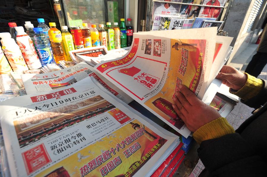 A pedestrian watches newspaper reporting the opening ceremony of the 18th National Congress of the Communist Party of China (CPC) in Beijing, capital of China, Nov. 8, 2012. 