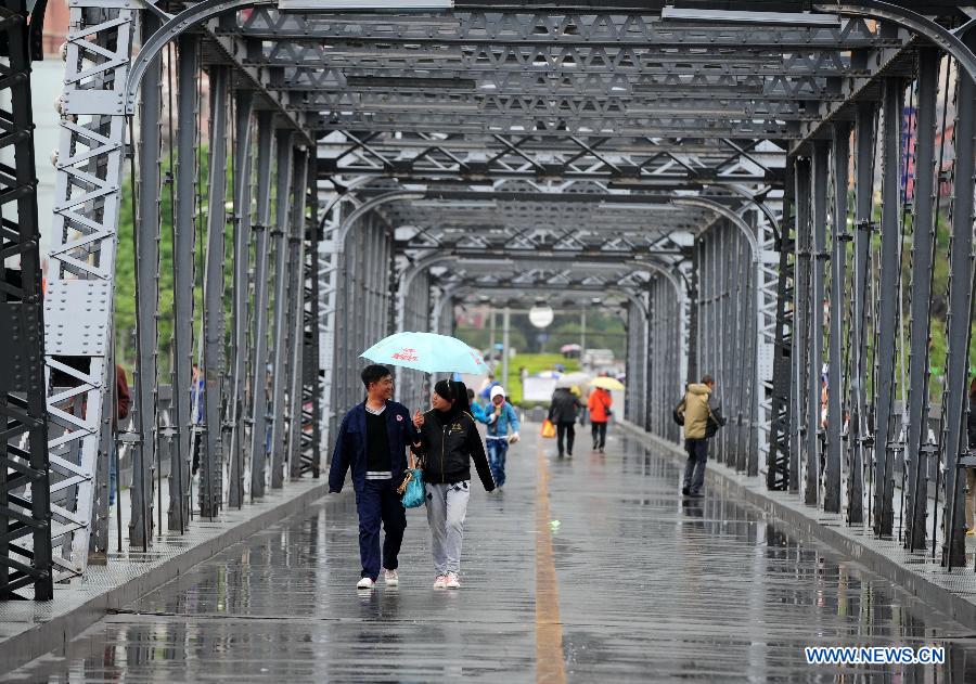 Citizens walk across a bridge in rain in Lanzhou, capital of northwest China's Gansu Province, May 8, 2013. 