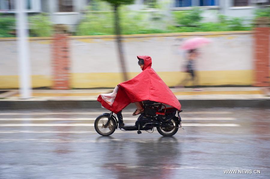 A woman rides electric bicycle in rain in Nanchang, capital of east China's Jiangxi Province, June 28, 2013.
