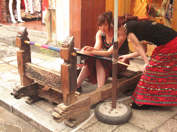 Two girls display how to weave local cotton cloth. With a history of over 1,400 years, West Street is located in the center of Yangshuo County and is also called Foreigner's Street. Here, the bars, hotels, Internet cafes and painting shops’ decoration style is mostly Chinese mixed with Western culture. [CnDG by Jiao Meng]