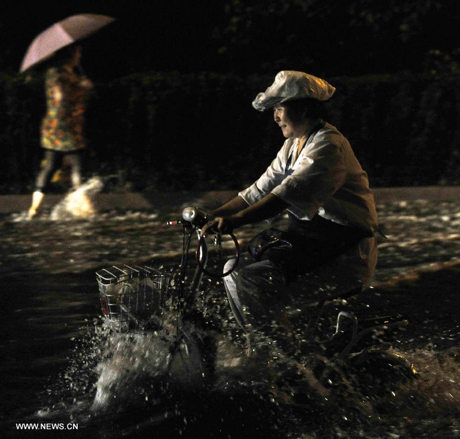 A citizen rides electric bicycle on a waterlogged road in Tianjin, north China, July 4, 2013.